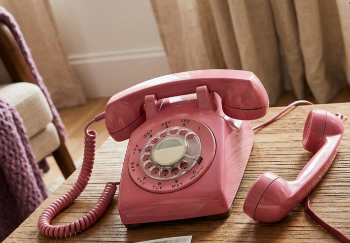Pink rotary phone beside photos, memory journal, tea, and lavender